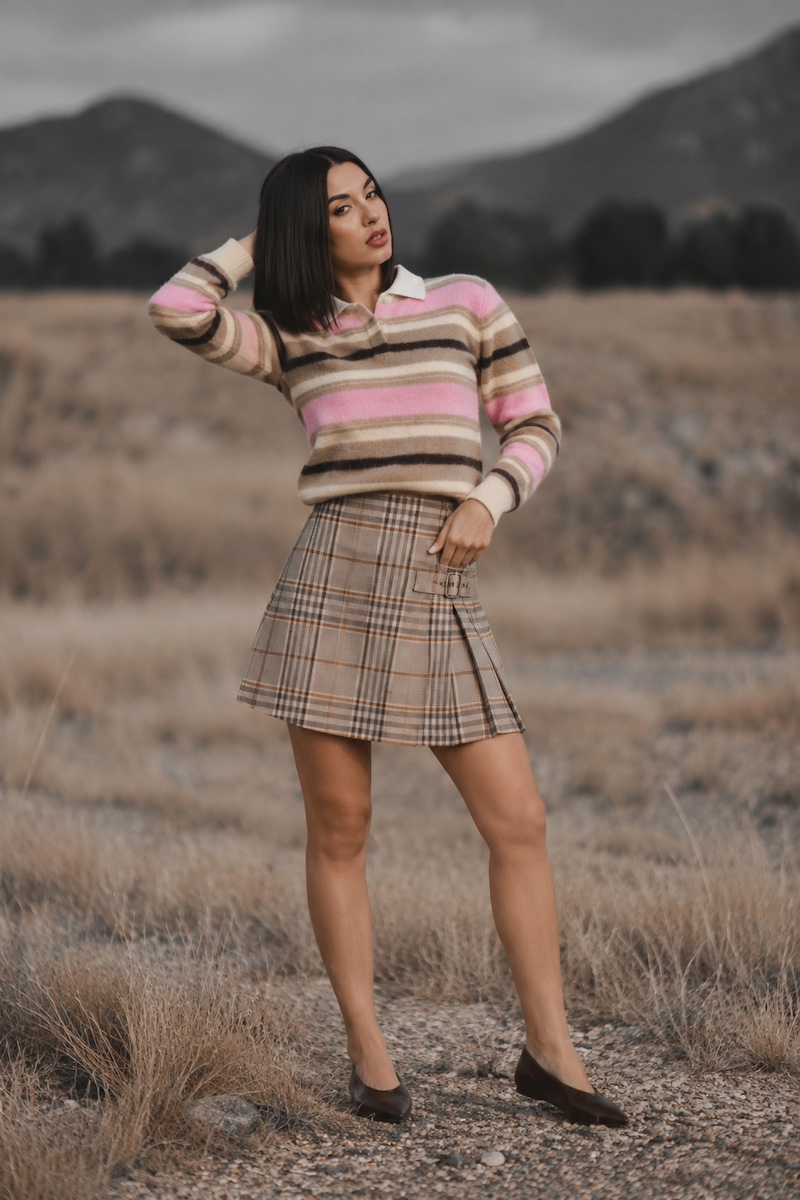 Model in a striped knit polo and a plaid mini skirt on a hillside